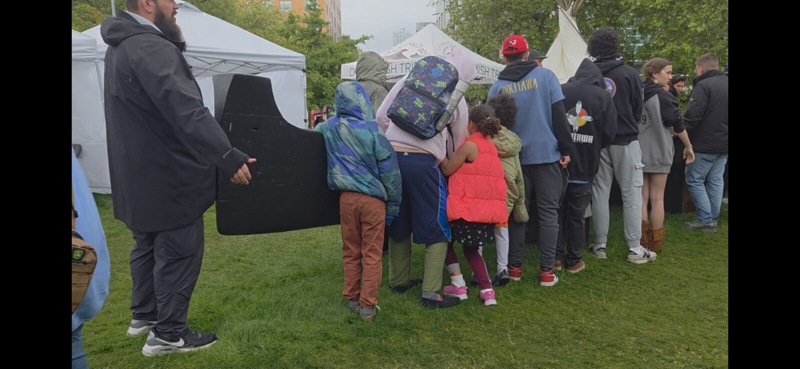 Youth gathered around the Makah-style whaling canoe at the Duwamish Tribe tent